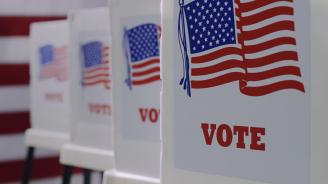 straight row of voting booths at polling station during American election. US flag in background.